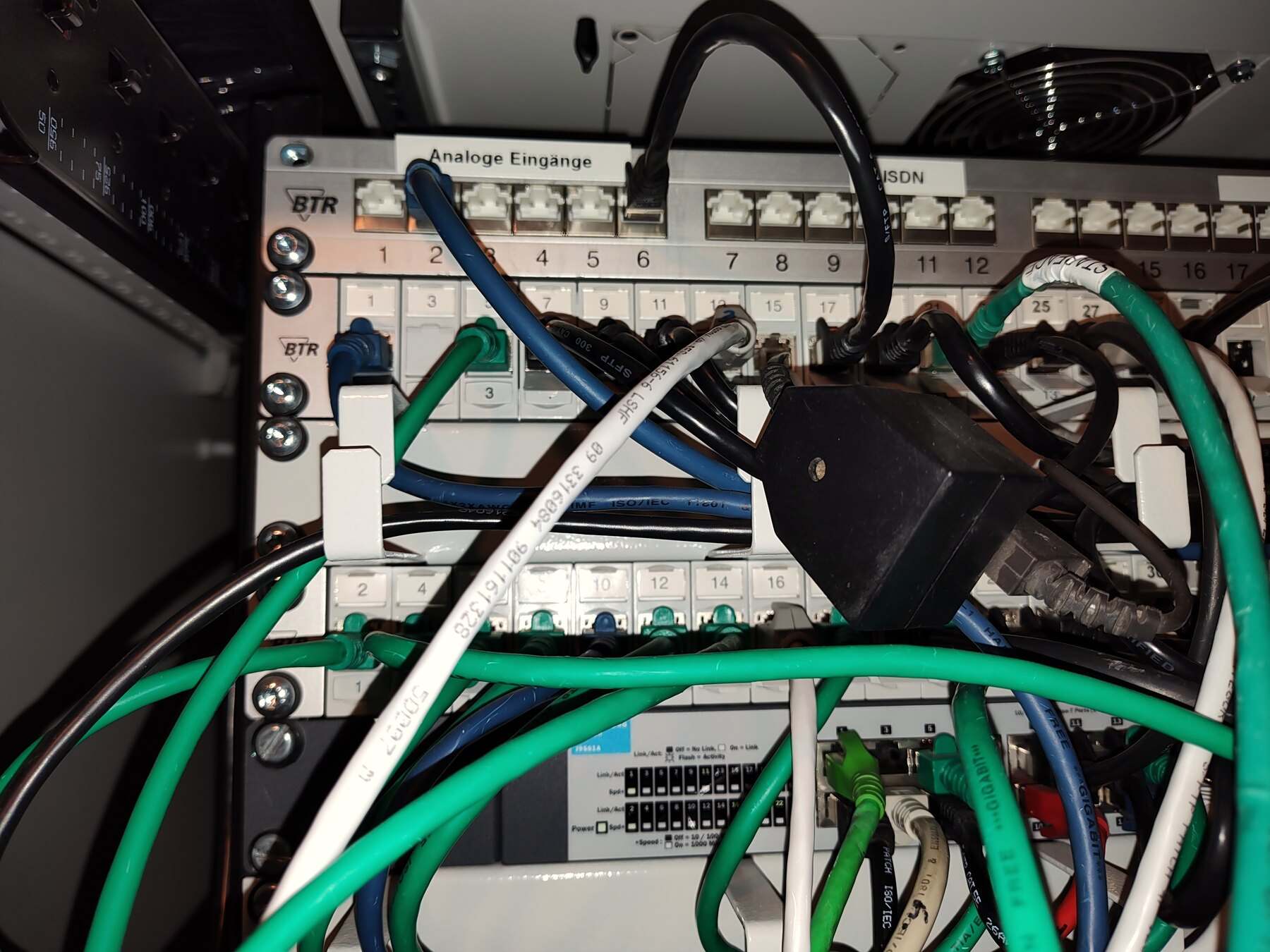 Gewachsener Netzwerkschrank im Bestand: Patchfeld mit analogen und ISDN-Eingängen, Patchkabel ohne Ordnung, Steckernetzteil im Schrank