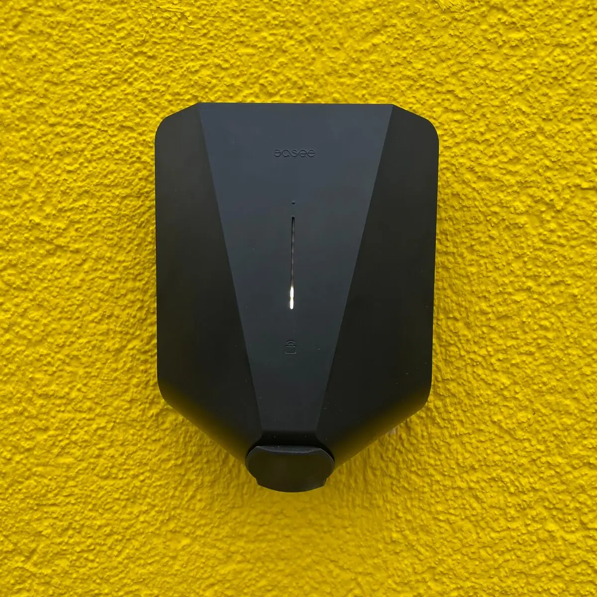 Schwarze Easee-Wallbox mit leuchtender Statusanzeige an einer gelb verputzten Wand